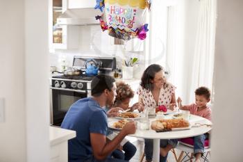 Young mixed race family having a birthday meal together at the table in their kitchen, seen from doorway