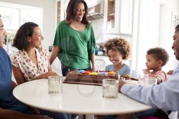 Three generation family mixed race family gathered around the kitchen table celebrating the pre-teen daughter’s birthday with a birthday cake