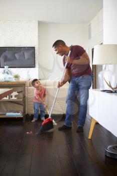Grandfather and his three year old grandson looking at each other while mopping and sweeping the dining room floor, full length, vertical