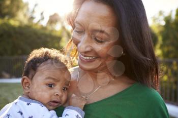 Happy mixed race middle aged grandmother holding her three month old grandson in the garden, close up, head and shoulders