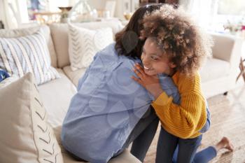 Pre-teen girl hugging her mother sitting on sofa in the living room, elevated, back view