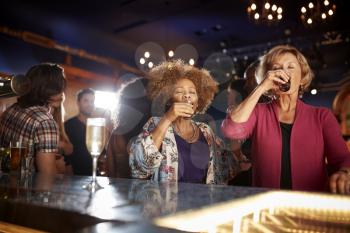 Female Senior Friends Drinking Shots In Bar Together