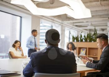 Rear View Of Business Professionals Meeting Around Table In Modern Office