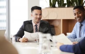 Businessman With Paperwork Sitting At Table Meeting With Colleagues In Modern Office