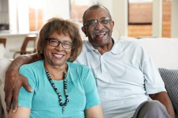 Senior black couple sitting at home, smiling to camera, close up