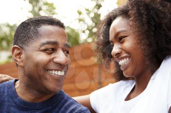 Middle aged black dad and teenage daughter smiling at each other, close up