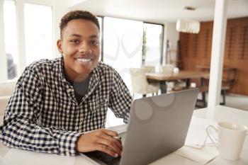 Black male teenager using a laptop computer at home smiling to camera, close up