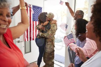 Millennial woman and family welcoming young black male soldier home, embracing in doorway, close up