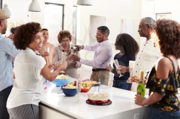 Middle aged black man pouring champagne to celebrate at home with his three generation family