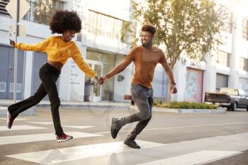 Fashionable young black couple running across a city street holding hands, full length, close up