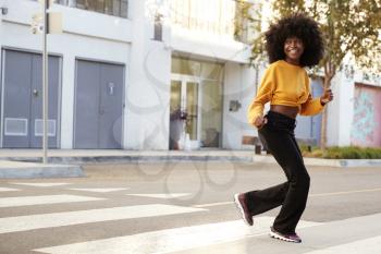 Fashionable young black woman with afro hair running across the street, full length, close up
