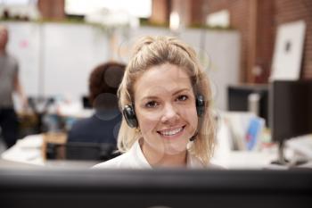 Portrait Of Female Customer Services Agent Working At Desk In Call Center
