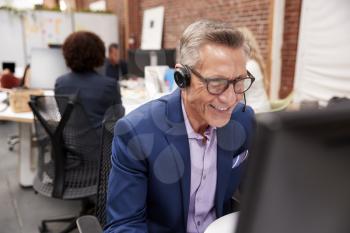 Mature Male Customer Services Agent Working At Desk In Call Center