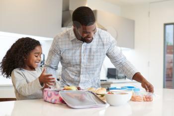 Daughter In Kitchen At Home Helping Father To Make Healthy Packed Lunch