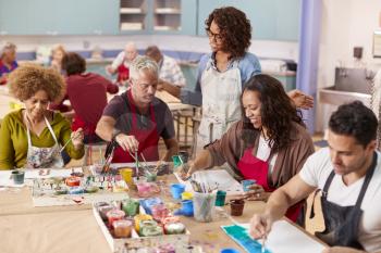 Group Of Mature Adults Attending Art Class In Community Centre With Teacher