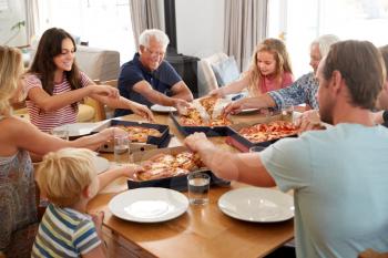Multi Generation Family Sitting Around Table Eating Takeaway Pizza Together