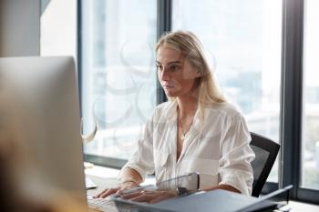 Young white blonde woman sitting at a desk working at a computer in a creative office, close up