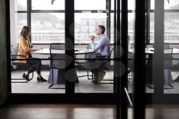 A businessman and young woman meeting for a job interview, full length, seen through glass wall