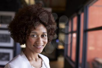 Millennial black businesswoman smiling to camera by the window in an office, close up