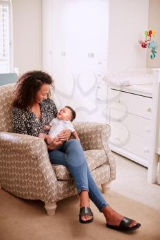 Loving Mother Sitting In Chair Cuddling Baby Son In Nursery At Home
