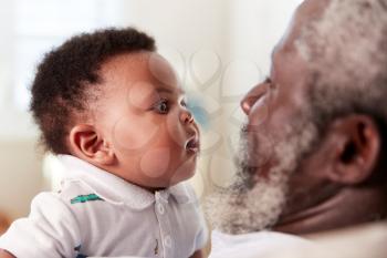 Proud Grandfather Cuddling Baby Grandson In Nursery At Home