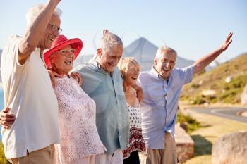 Senior Friends Visiting Tourist Landmark On Group Vacation With Arms Raised