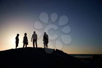 Silhouette Of Senior Friends Standing On Rocks By Sea On Vacation At Sunset