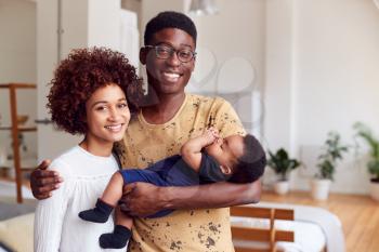 Portrait Of Loving Parents Holding Newborn Baby At Home In Loft Apartment