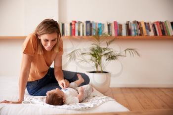 Loving Mother With Newborn Baby Lying On Bed At Home In Loft Apartment
