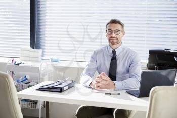 Portrait Of Mature Male Doctor Sitting Behind Desk In Office