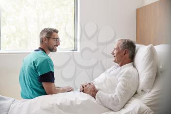 Surgeon Visiting And Talking With Senior Male Patient In Hospital Bed In Geriatric Unit