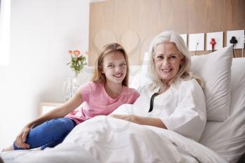 Portrait Of Granddaughter Visiting Grandmother In Hospital Bed