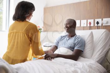 Wife Visiting And Talking With Patient Husband In Hospital Bed