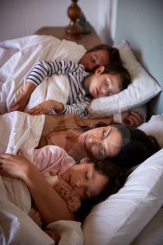 Mid adult parents and their two young children lying asleep in bed, waist up, close up, vertical
