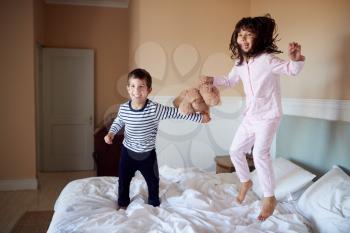 Brother and sister having fun bouncing on their parents’ bed in their pyjamas, full length