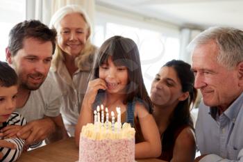 Three generation white family celebrating young girl’s birthday with a cake and candles, close up