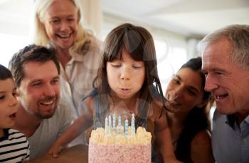 Six year old white girl blowing out the candles on birthday cake watched by her family, close up