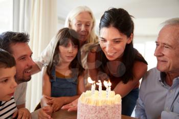 Six year old girl blowing out the candles on birthday cake watched by her mum and family, close up