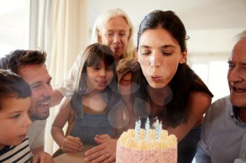Mid adult white woman blowing out candles on birthday cake watched by her family, close up