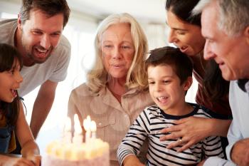 Senior white woman celebrating her birthday with family, blowing out candles on her cake, close up