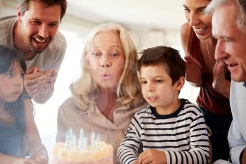 Senior white woman celebrating her birthday with family blowing out the candles on her cake