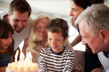 Four year old white boy and his family celebrating his birthday with cake and lit candles, close up