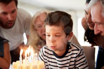 Four year old white boy celebrating with family blowing out candles on his birthday cake, close up