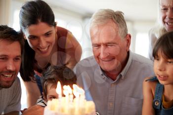 Senior white man and his family celebrating his birthday with cake and lit candles, close up