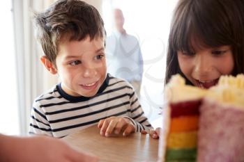 Young siblings looking at a colourful sliced birthday cake on a table, close up, selective focus