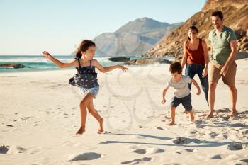 Happy young white family on holiday exploring a beach together, full length