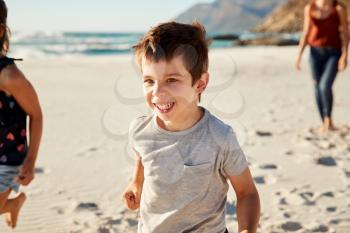 Four year old white boy on holiday with his family running on the beach, close up