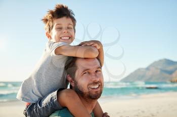 Mid adult white man on a beach with four year old son on his shoulders, looking to camera, close up