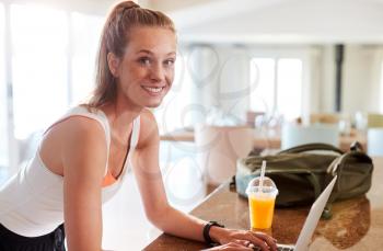 Millennial white woman checking fitness app on her laptop after gym smiling to camera, side view