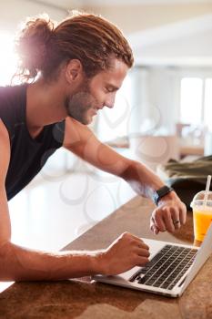 Millennial white man checking fitness app on watch and laptop after a workout, side view, vertical
